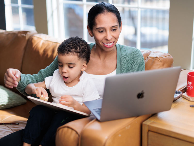 A mother works on her laptop as she holds her child on her lap