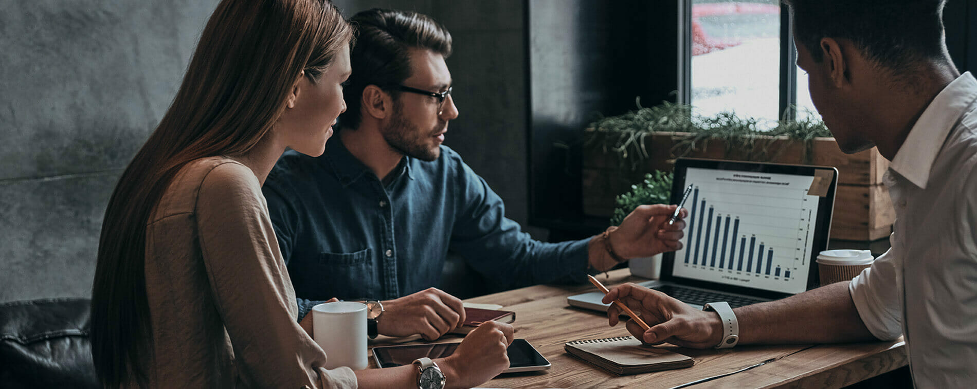 Three business professionals looking at a column chart on a laptop screen.