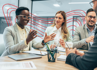 Three colleagues engaged in a collaborative discussion around a table, smiling and gesturing during a team meeting.