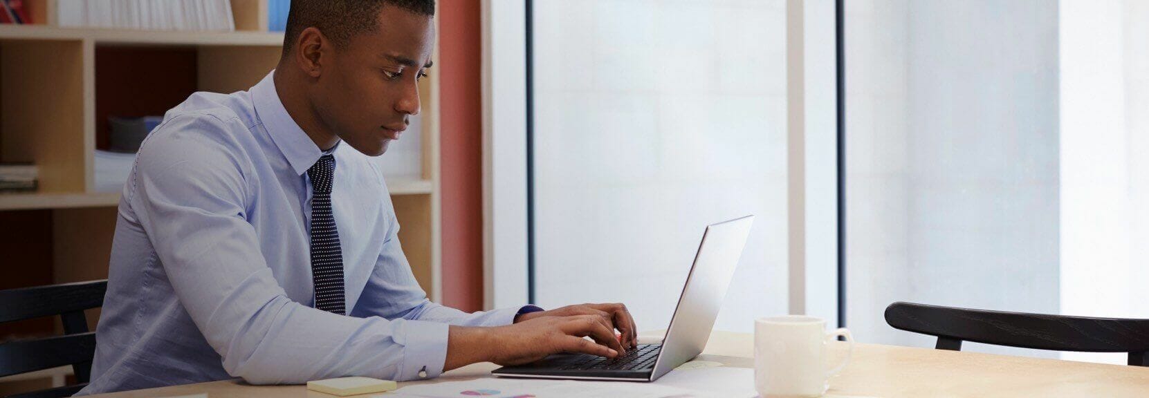 A business professional working on a laptop in an office setting.