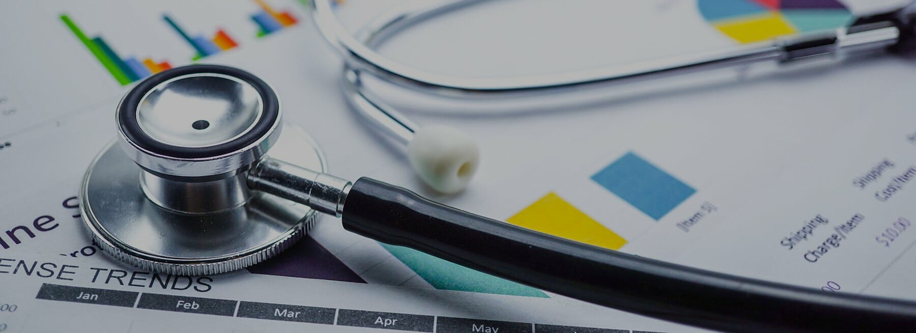 A closeup image of a stethoscope laying across a pile of financial documents.