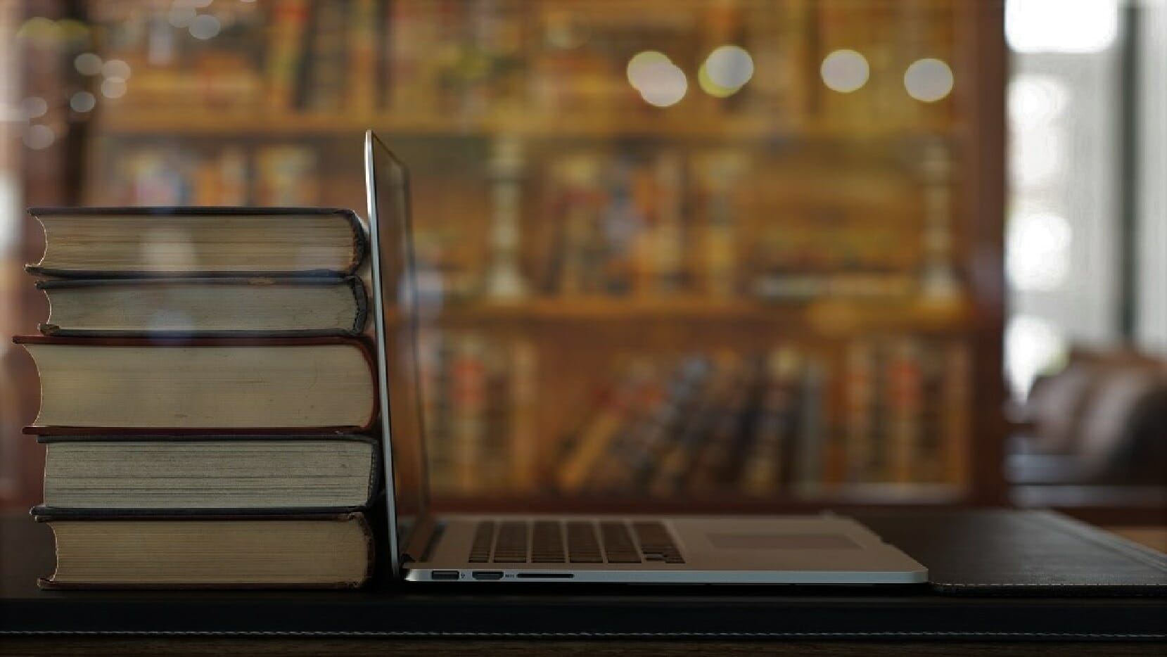 An open laptop sitting on a table in front of a stack of legal textbooks.