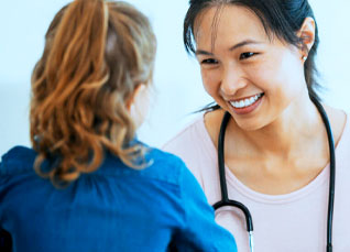 A woman wearing a stethoscope smiles at a child patient.
