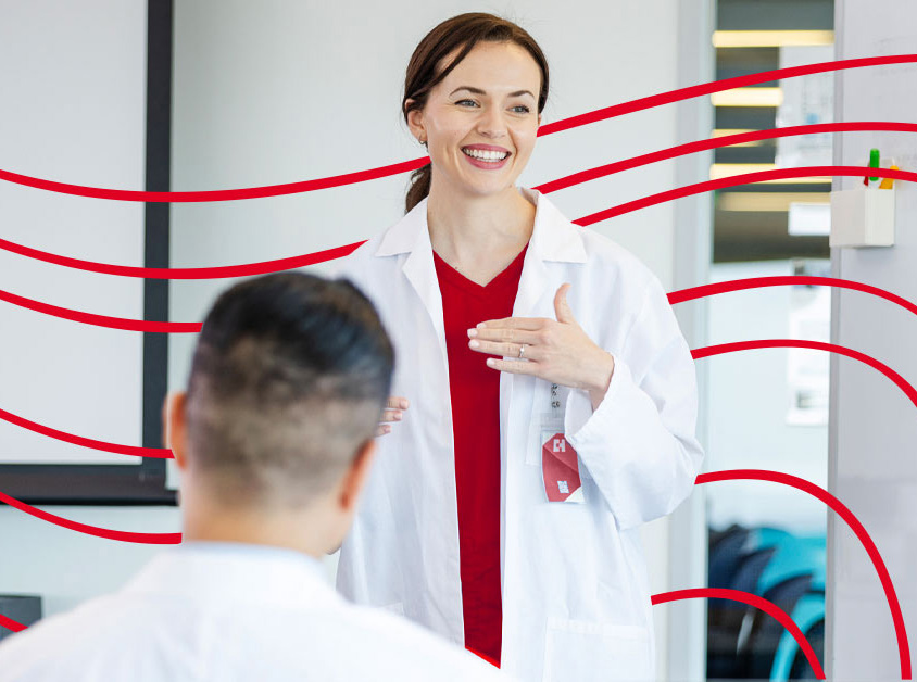 Nurse wearing white lab coat and red scrubs teaching a group class