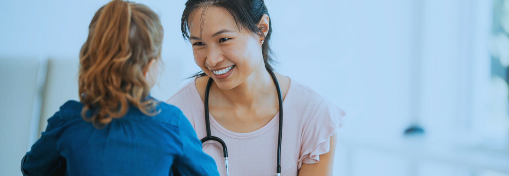 A woman wearing a stethoscope smiles at a child patient.
