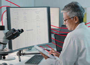 Professional reviewing compliance data on a desktop monitor in a laboratory office.
