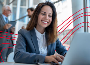 Professional smiling while working on a laptop in a bright office setting.