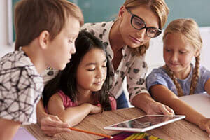 Teacher interacting with three students with a tablet.