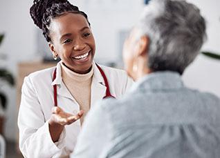 DNP in white lab coat with red stethoscope talking with an older female patient