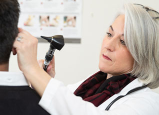 Nurse practitioner examining patient’s ear in clinical setting.