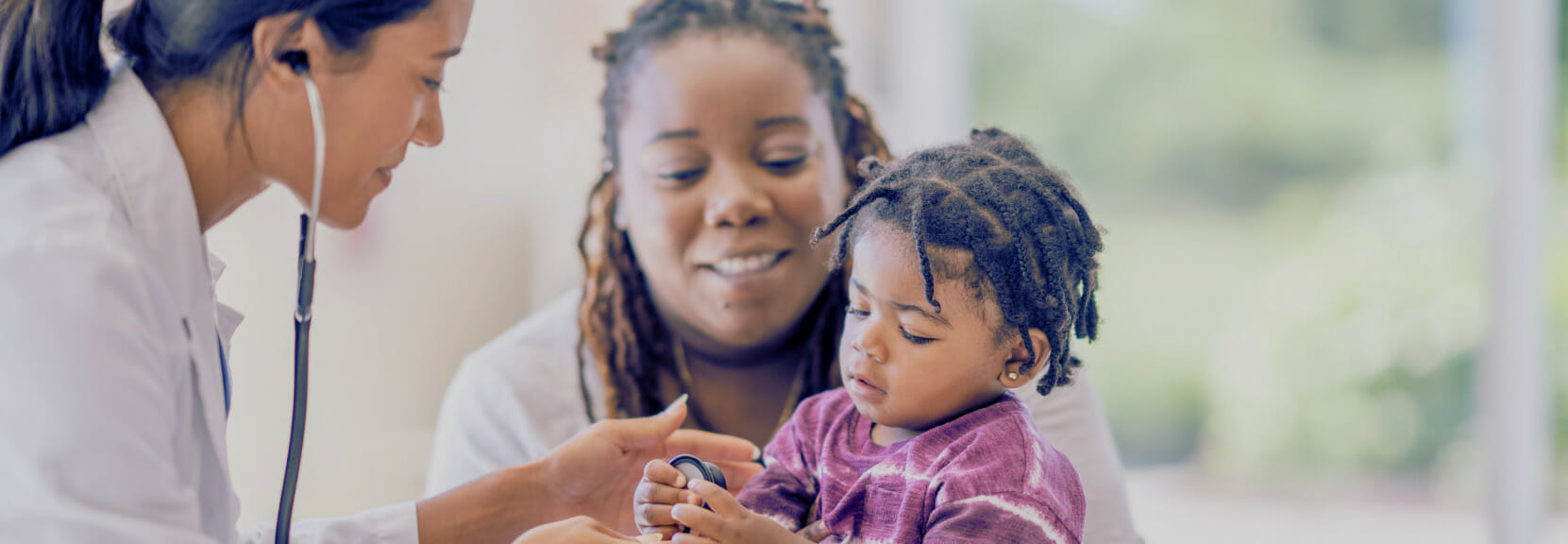Nurse examining a child held by parent in a clinic.