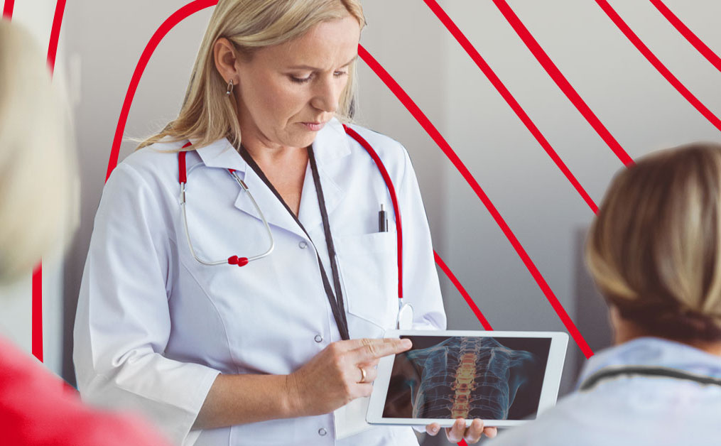 Group of nursing students and instructor discussing a spine model during an anatomy lesson in a classroom setting.