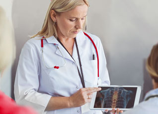 Group of nursing students and instructor discussing a spine model during an anatomy lesson in a classroom setting.