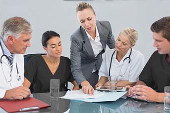 MSN nurse leader instructing fellow nurses while overlooking a document on a table.