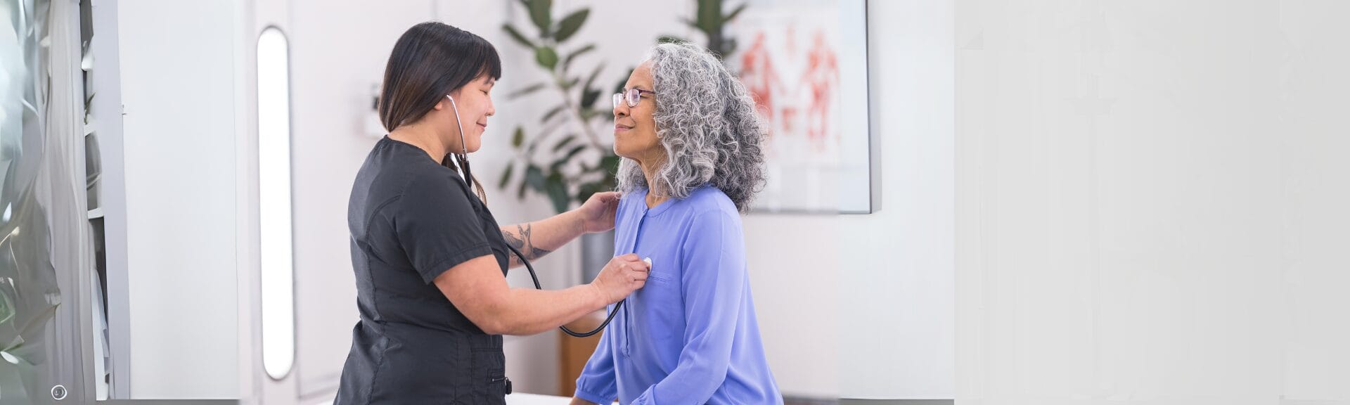 Nurse practitioner performing a checkup with a stethoscope on an older female patient during a routine wellness visit in a clinic.