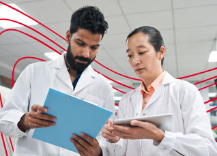 Two healthcare researchers reviewing patient data on a clipboard and tablet in a clinical setting.