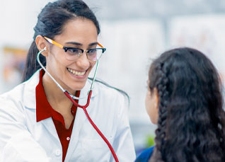 RN in red scrubs and white lab coat smiling and examining a young girl patient.