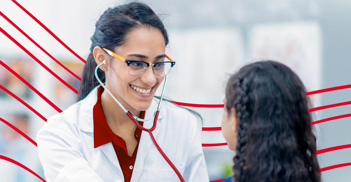 RN in red scrubs and white lab coat smiling and examining a young girl patient.