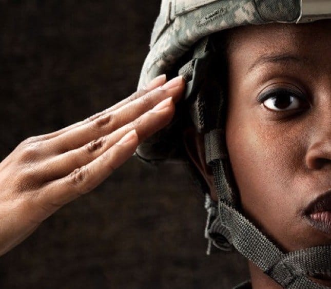 This close-up image shows a military service member facing the camera and saluting with her right hand and half of her face in frame..