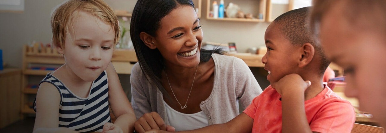 Early childhood educator smiles with two young students. 