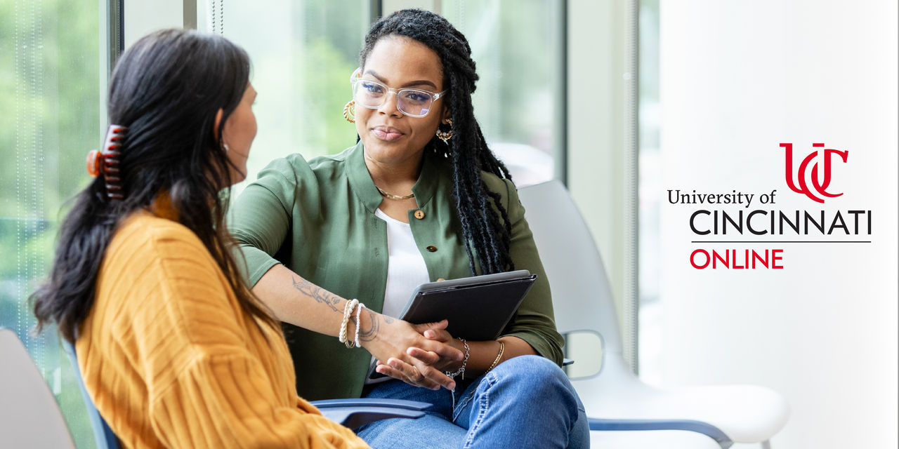 female advisor wearing a green cardigan holding an ipad sitting in a chair facing a prospective female student wearing a yellow shirt