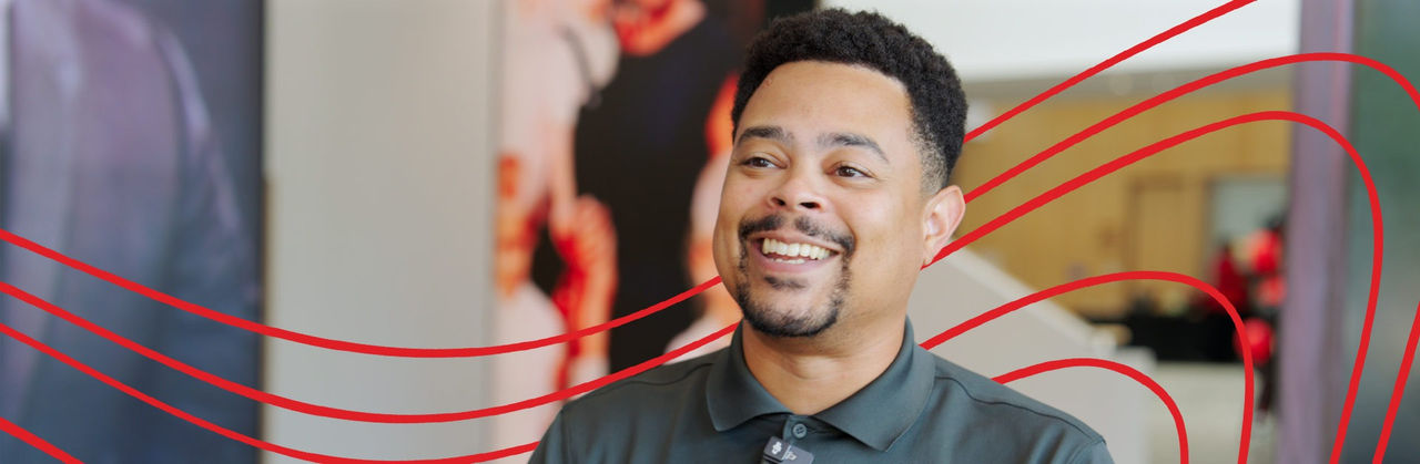 Faculty member Kris Jones, a black man with short hair and a goatee, sits in an academic building. He wears a dark polo shirt and is smiling.