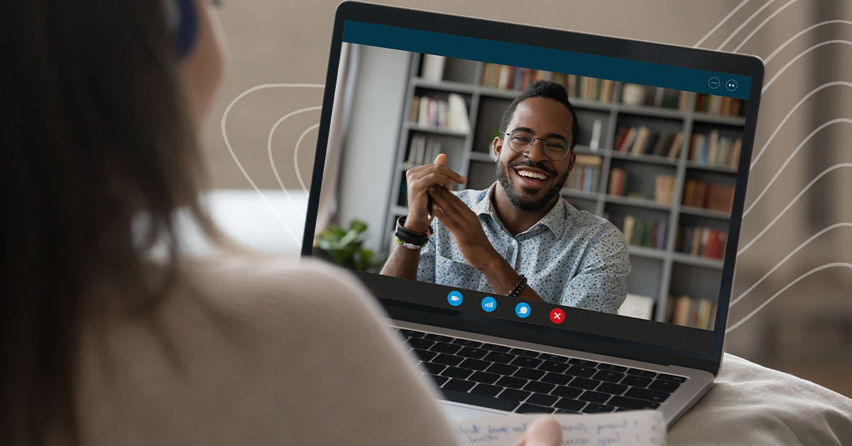 A woman speaks to a male online college staff member on a video call on her laptop screen. The man is black, wears a light blue polo shirt, and smiles with his hands clasped in front of him.