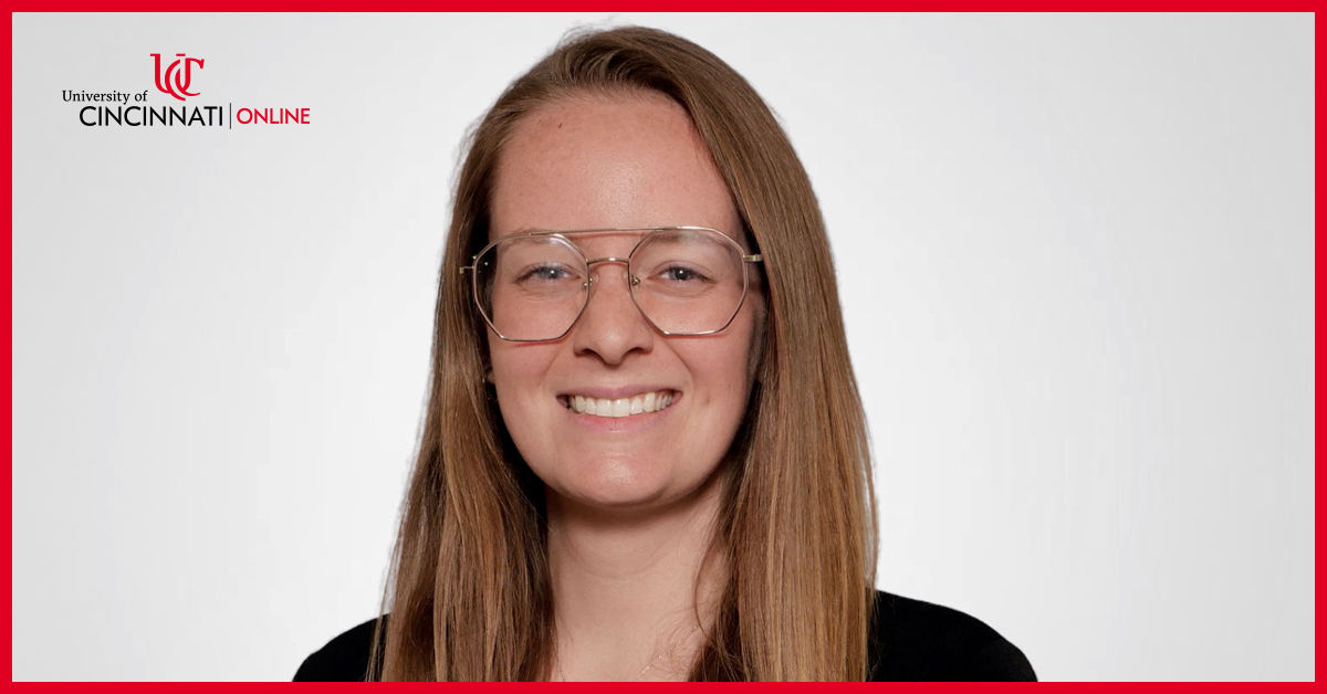 UC online graduate Hanna Freeman smiles in front of a white background. She is white, has long light brown hair, and wears large wire-rimmed glasses.