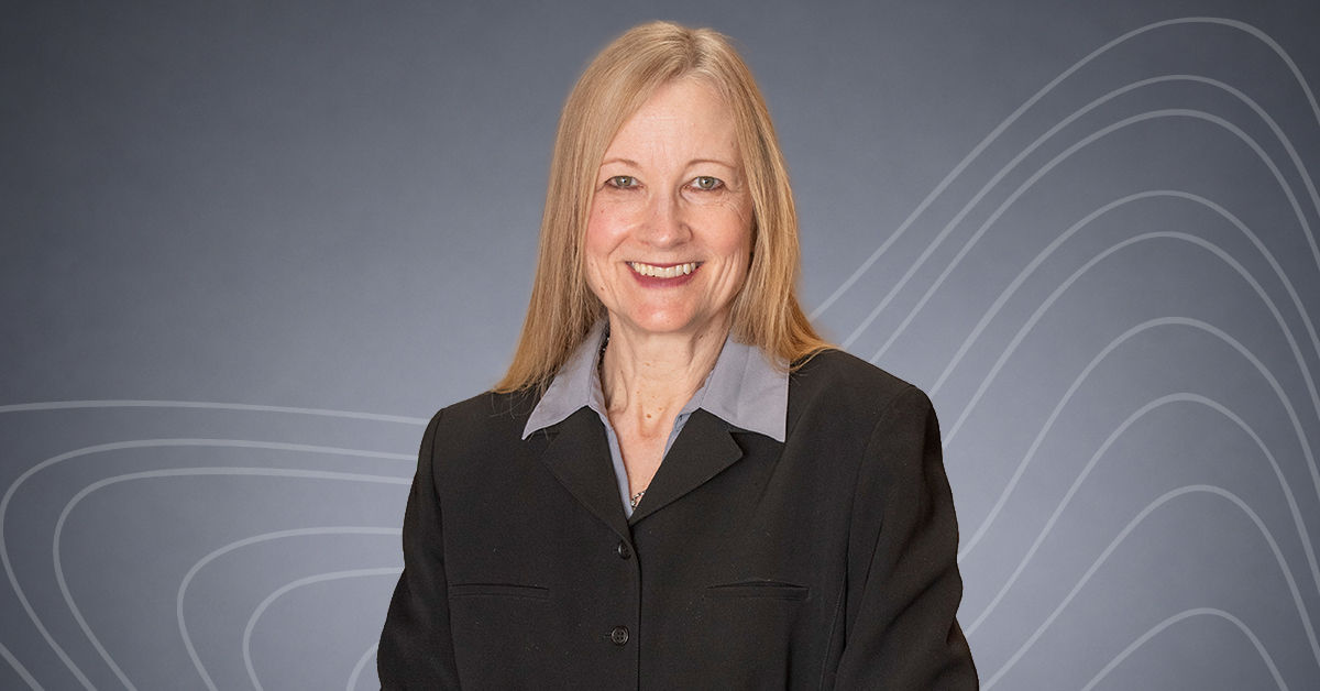 UC Master of Legal Studies Program Director Susan Stephan stands and smiles in front of a gray background. She wears a black blazer and has light long blonde hair.