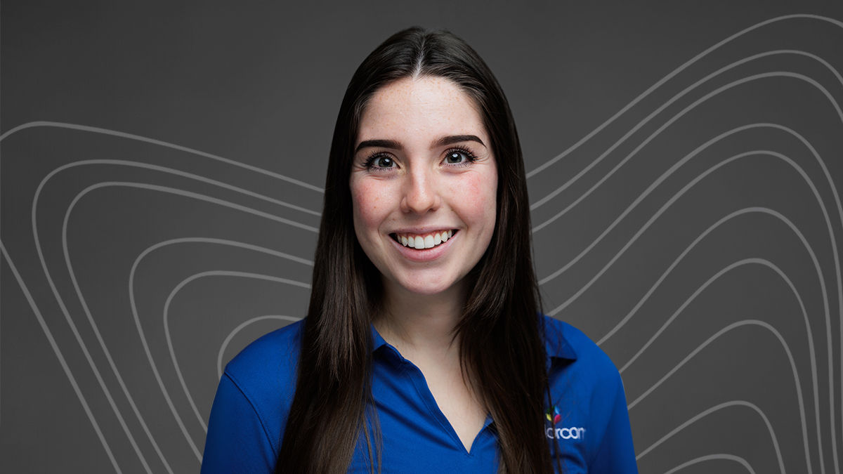 UC Online master’s in marketing student Ariana Keller smiles in front of a gray background. She is white, has long black hair, and wears a blue polo shirt.