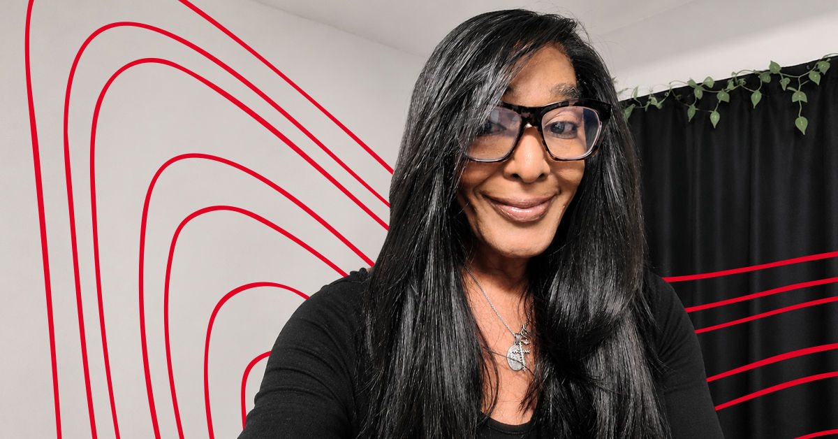 UC Online Bachelor of Social Work student Cassandra Ellis wears a black shirt and black glasses in front of black curtains and a beige wall background.