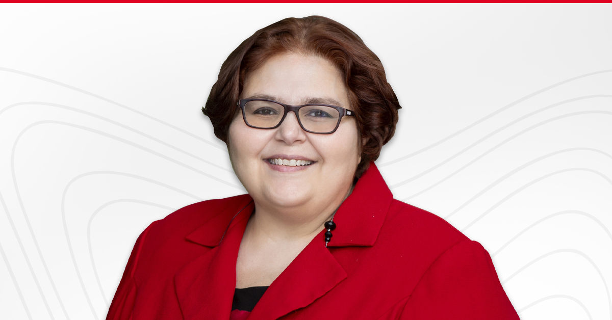 Dr. Demetra Castillo, a University of Cincinnati Online professor, wears a red blazer and smiles forward. She wears dark glasses and has short, wavy dark brown hair.