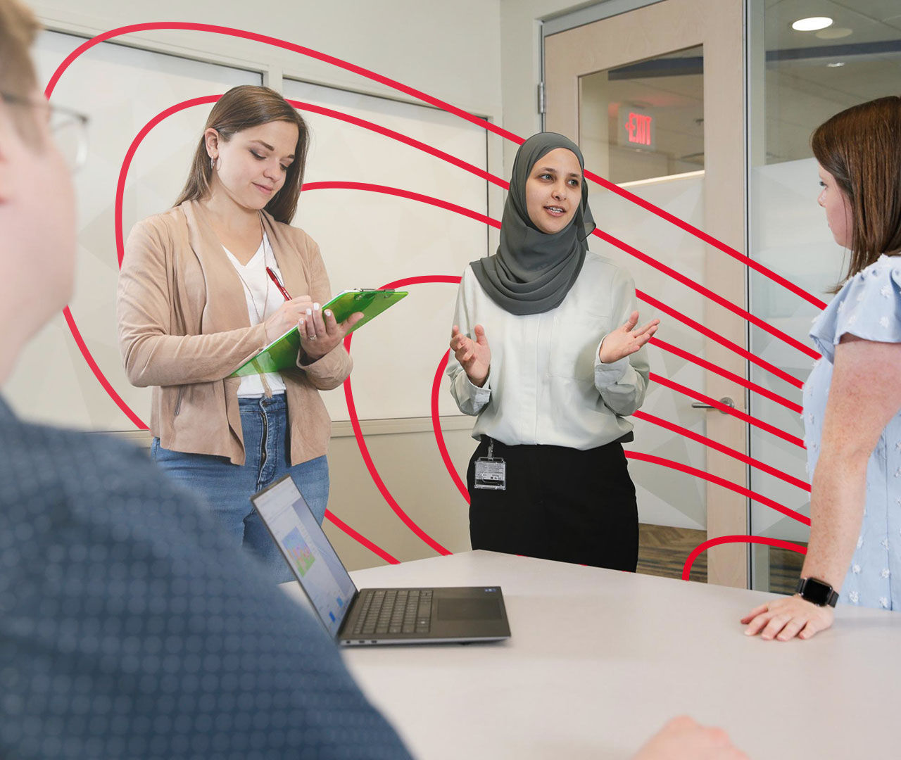 four coworkers in a conference room discussing a project on a laptop and taking notes