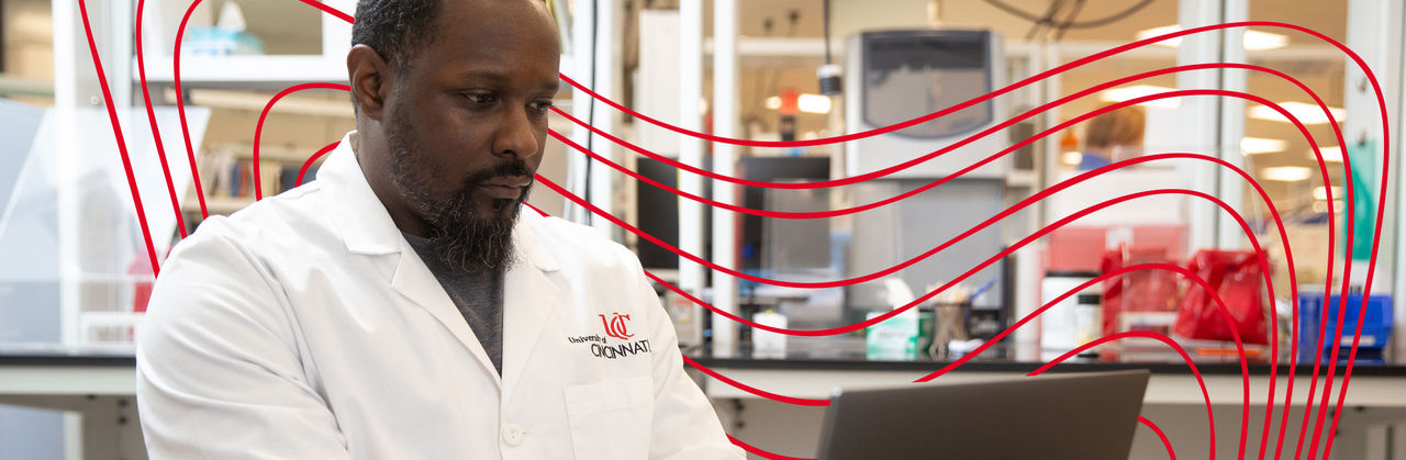 Two medical laboratory science professionals wearing University of Cincinnati lab coats discussing test results in a modern clinical laboratory.