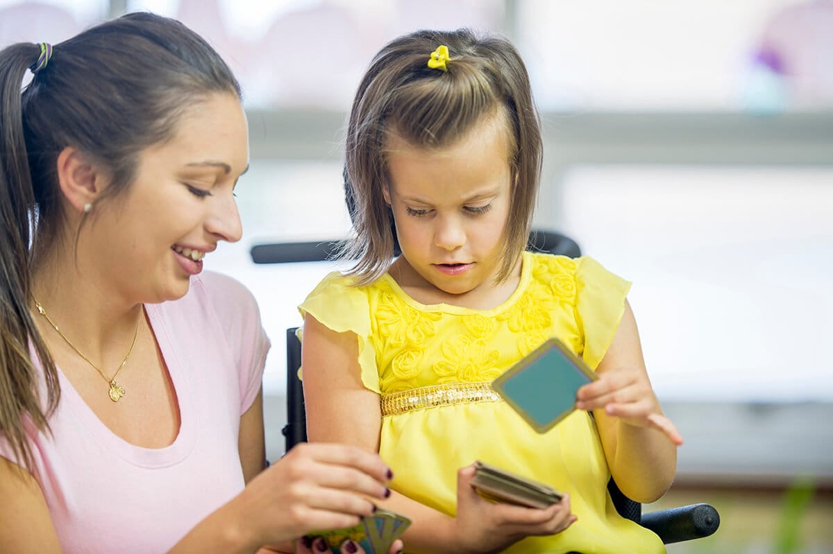 A teacher playing card games with a child in classroom setting.