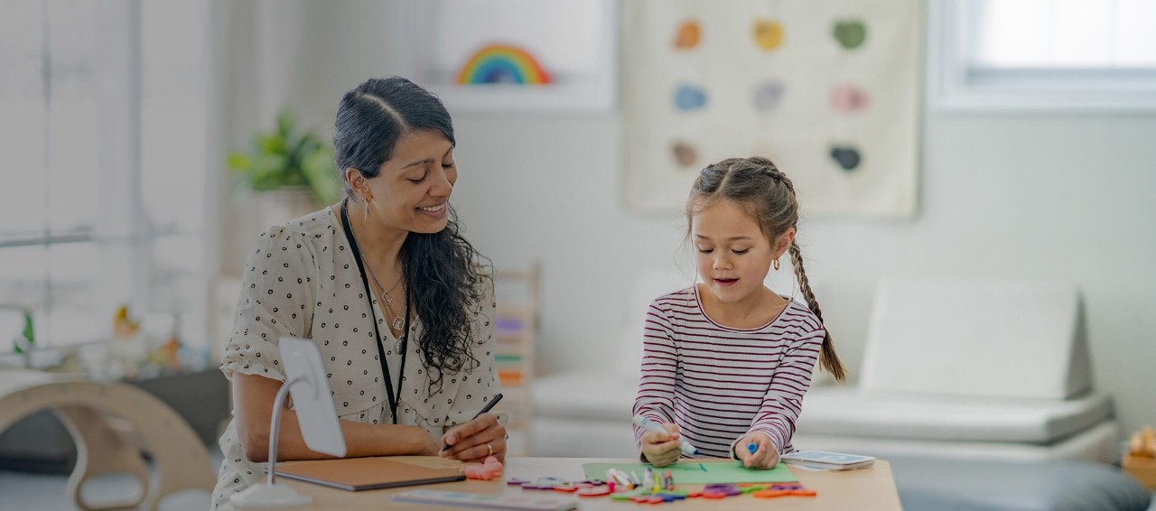 Behavior analyst engaging with a child in classroom setting. The child is drawing a picture with a blue marker.