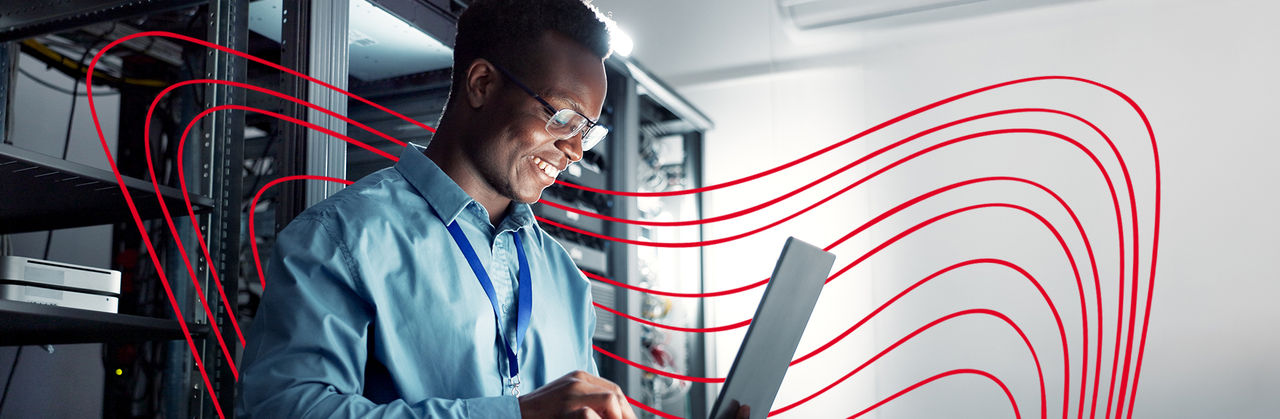An IT professional works on a laptop in a server room, managing systems and analyzing technical infrastructure.