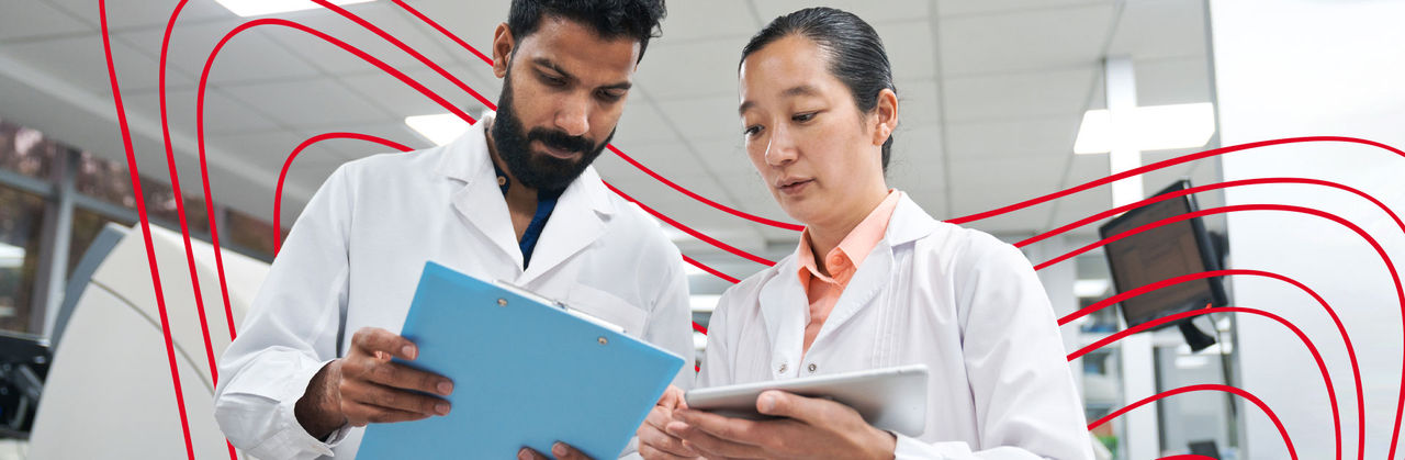 Researchers in a dimly lit laboratory discussing data beside microscopes and lab instruments, symbolizing health outcomes and pharmacoeconomics research.