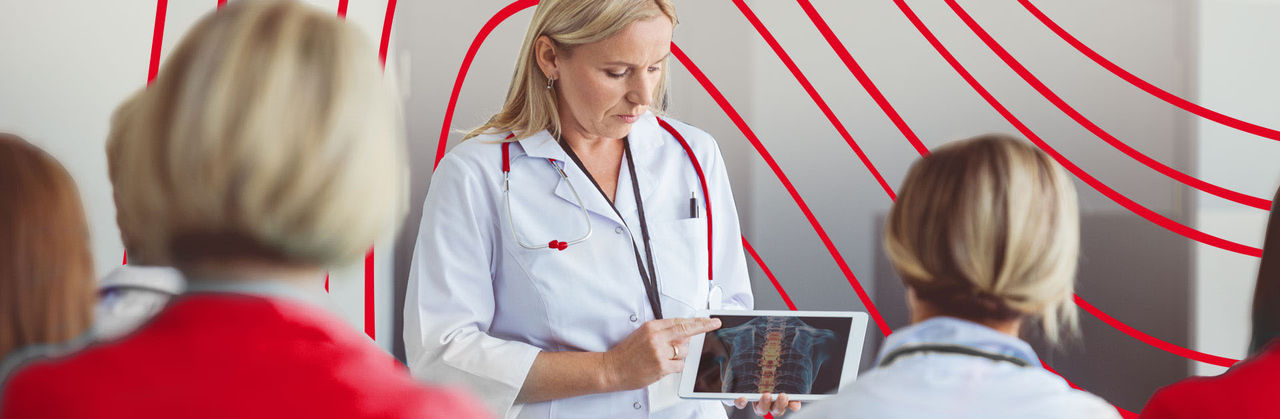 Group of nursing students and instructor discussing a spine model during an anatomy lesson in a classroom setting.