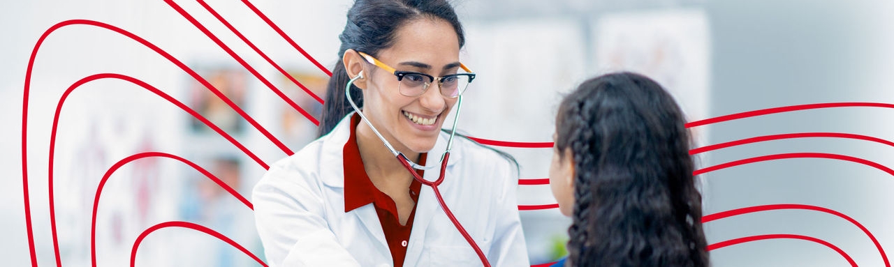 An RN to BSN wearing a white coat and red stethoscope listening to a child's heartbeat