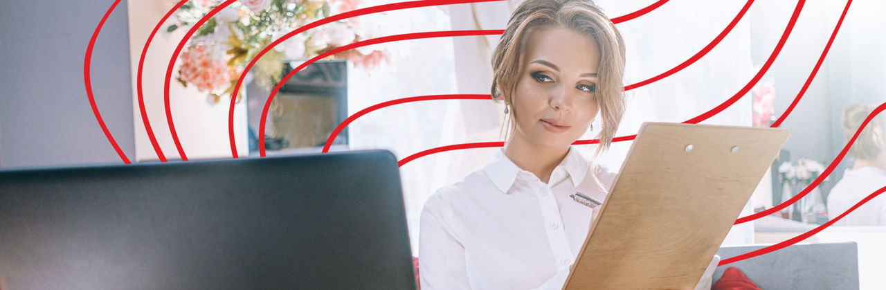 Hospitality management professional observes a computer screen while writing on a clipboard.