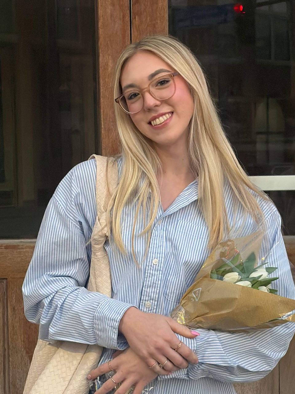Anna Black poses for a headshot. She is a blonde woman with a blue collared shirt holding a bouquet of flowers.