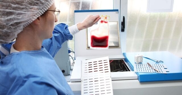 Lab scientist holding and observing a blood bag.
