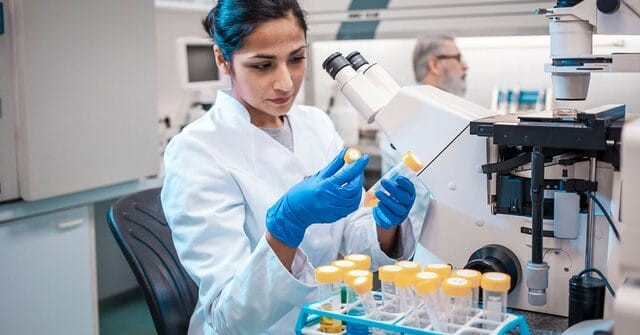 Microbiologist examining vials.