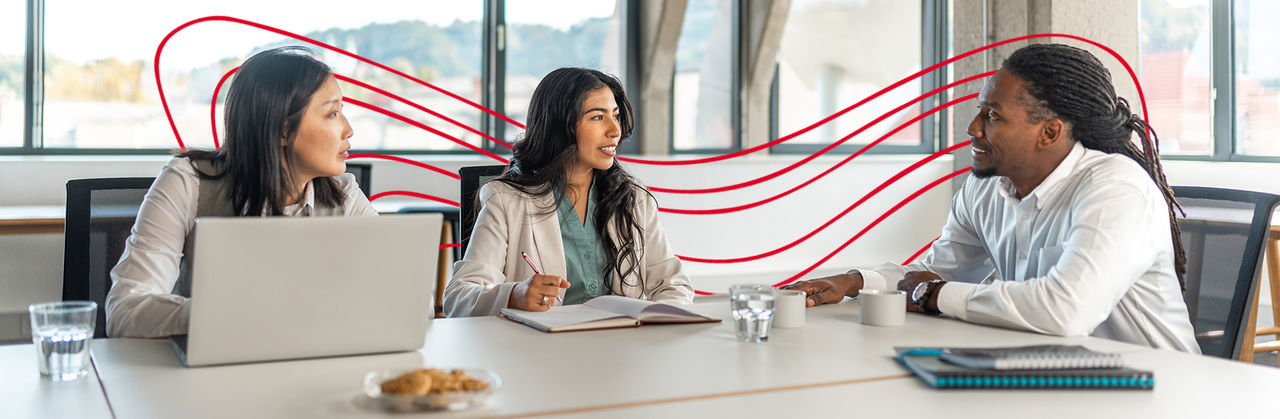 Three professionals meet at a table, discussing ideas and taking notes during a business planning session.