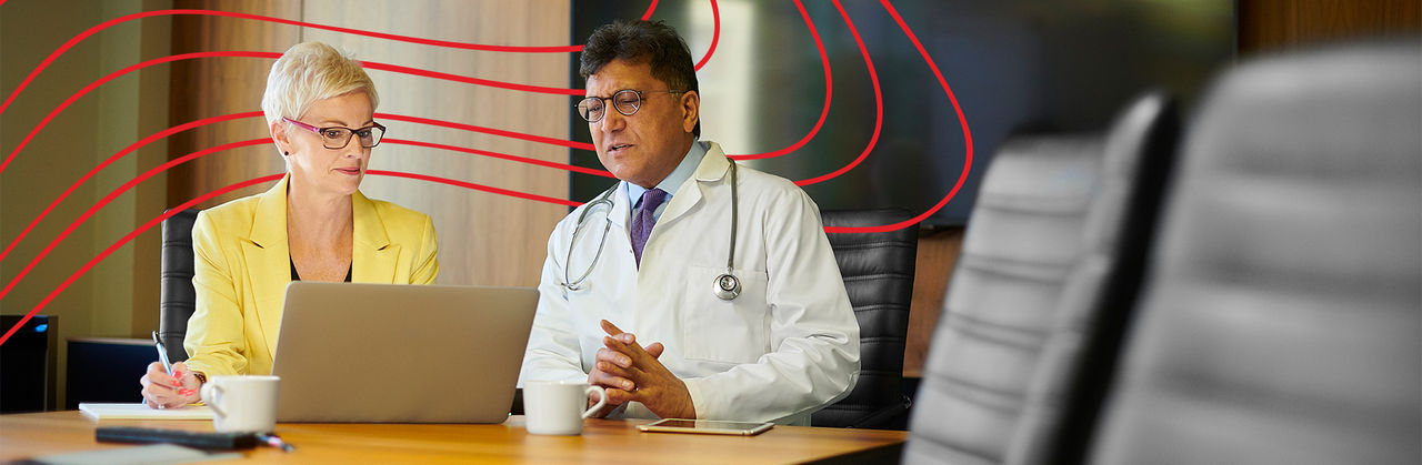 A group of health professionals sits at a meeting table speaking with each other. There are five people at the table.