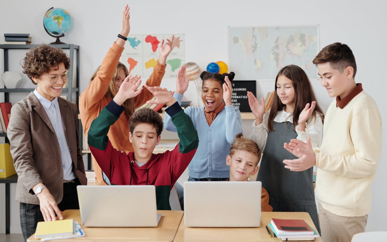 Sustainability educator with a group of students who have their hands raised celebrating and clapping.